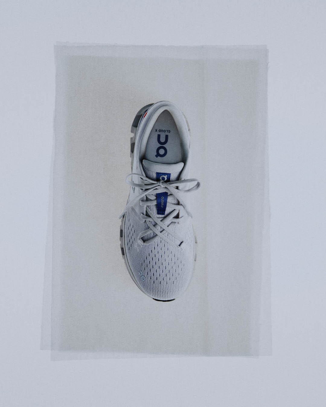 Top-down view of a white On Cloud running shoe with tied laces and breathable mesh upper on pale background