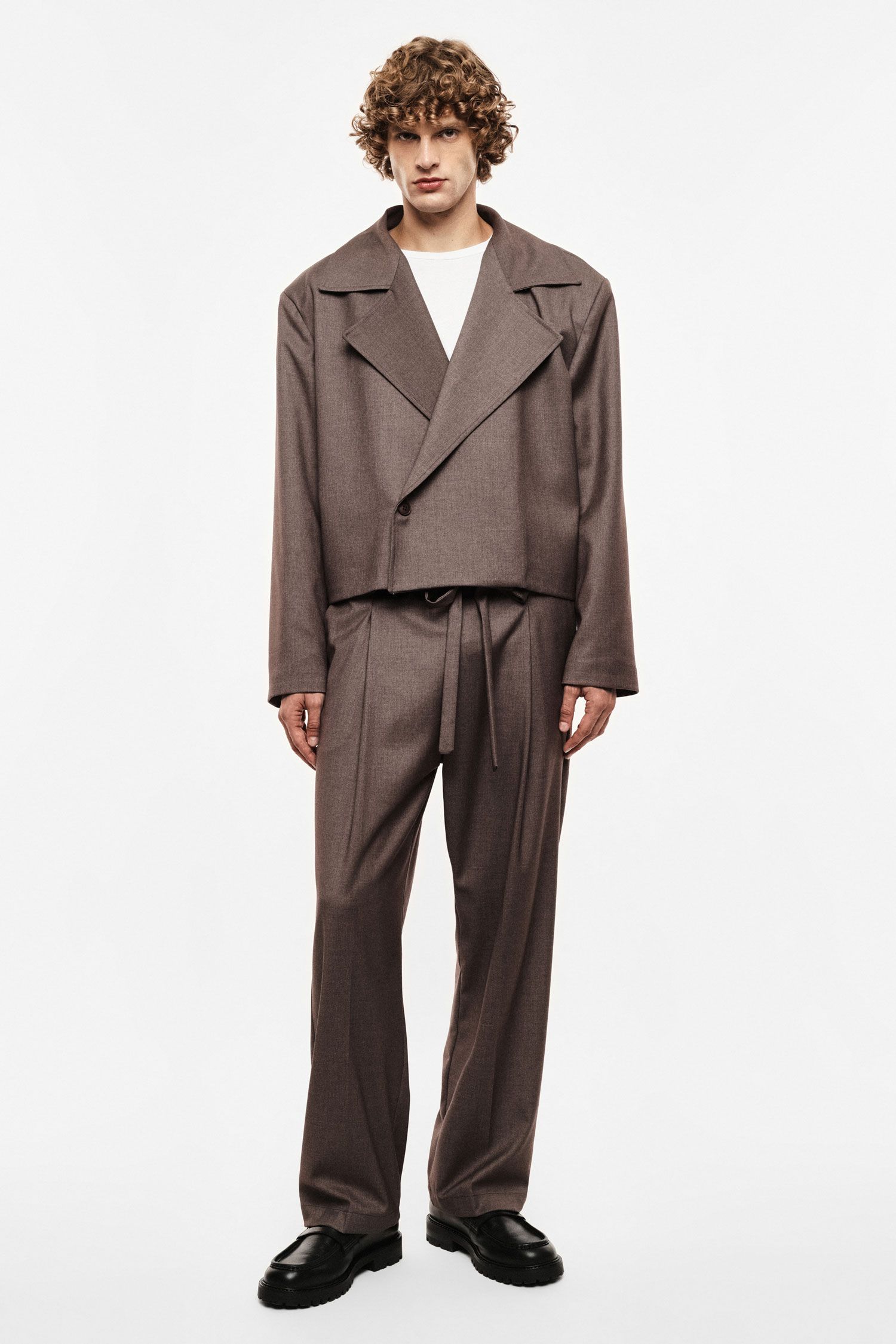 Model wearing brown cropped double-breasted blazer, matching high-waist wide-leg trousers and black loafers on white background