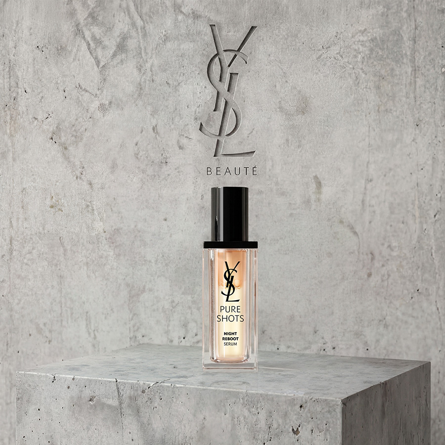 Un flacone di siero YSL Pure Shots Night Reboot esposto su un piedistallo di cemento sotto un logo YSL Beaut&eacute; inciso.