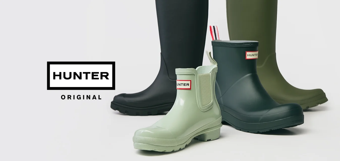 Quattro paia di stivali da pioggia Hunter in nero, verde scuro, verde chiaro e blu marino, disposti su uno sfondo bianco.