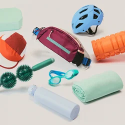 Casco da bici blu, rullo in schiuma arancione, cappellino rosso, marsupio marrone, rullo da massaggio verde, occhialini da nuoto blu, borraccia, asciugamano e saponetta su sfondo bianco.