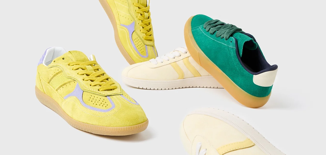 Quattro paia di sneakers: scamosciate gialle con dettagli viola, crema con strisce gialle, scamosciate verdi con tallone blu scuro e suola bianca.