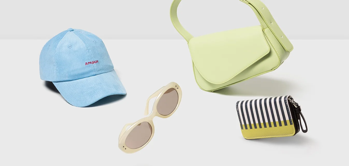 Cappello celeste, borsa a tracolla giallo-verde, occhiali da sole bianchi e una pochette a strisce nera e gialla su uno sfondo bianco.