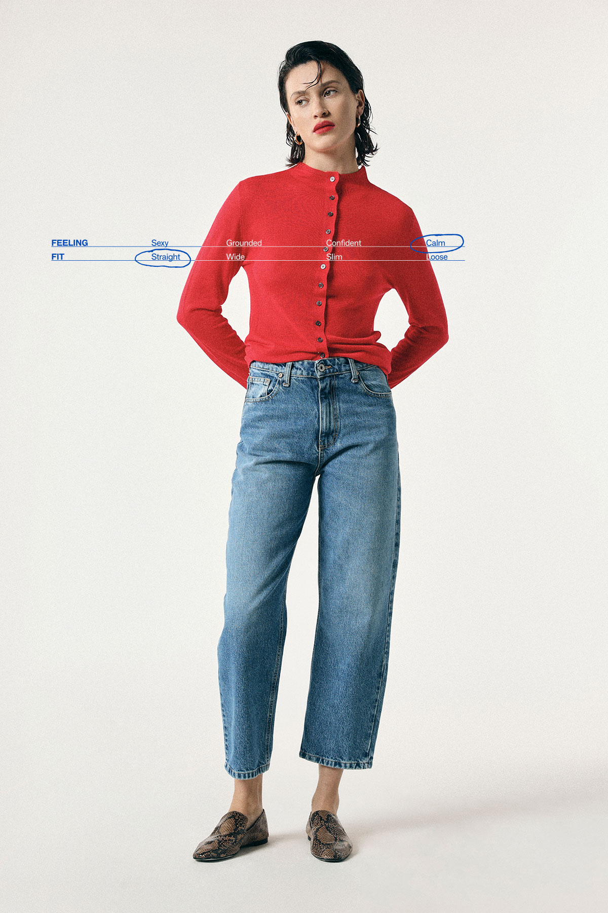 Woman modelling red buttoned cardigan, high‑waist cropped blue jeans and patterned loafers, hands behind back against plain white background