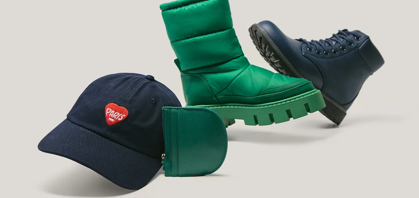 Cappello della Marina con logo a cuore rosso, stivale invernale imbottito verde, piccolo portafoglio verde e scarponcino blu scuro con lacci su sfondo chiaro.