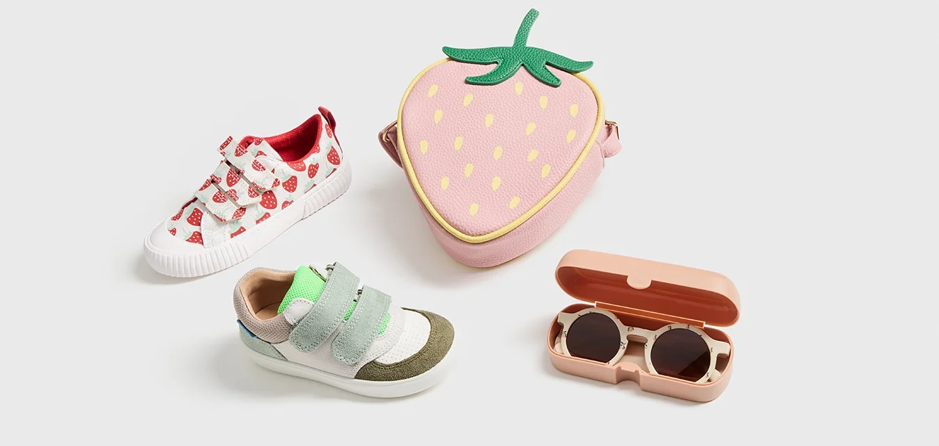 Scarpe bianche con motivi a fragola rossi, scarpe velcro verdi e grigie, una borsa a forma di fragola rosa e un astuccio per occhiali da sole rosa.