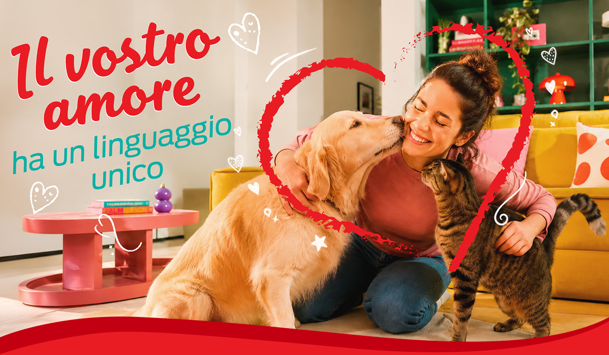 Donna sorridente abbraccia il suo cane e il suo gatto in salotto con testo 'il vostro amore ha un linguaggio unico'.