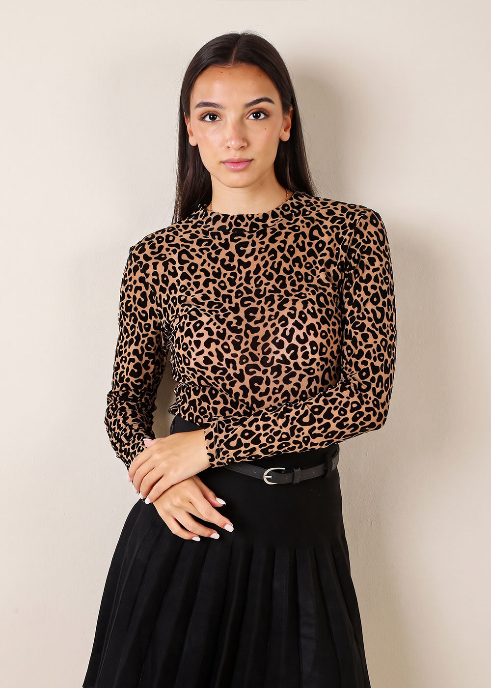 Woman wearing a leopard-print long-sleeve top and black pleated skirt with belt, standing against a neutral background