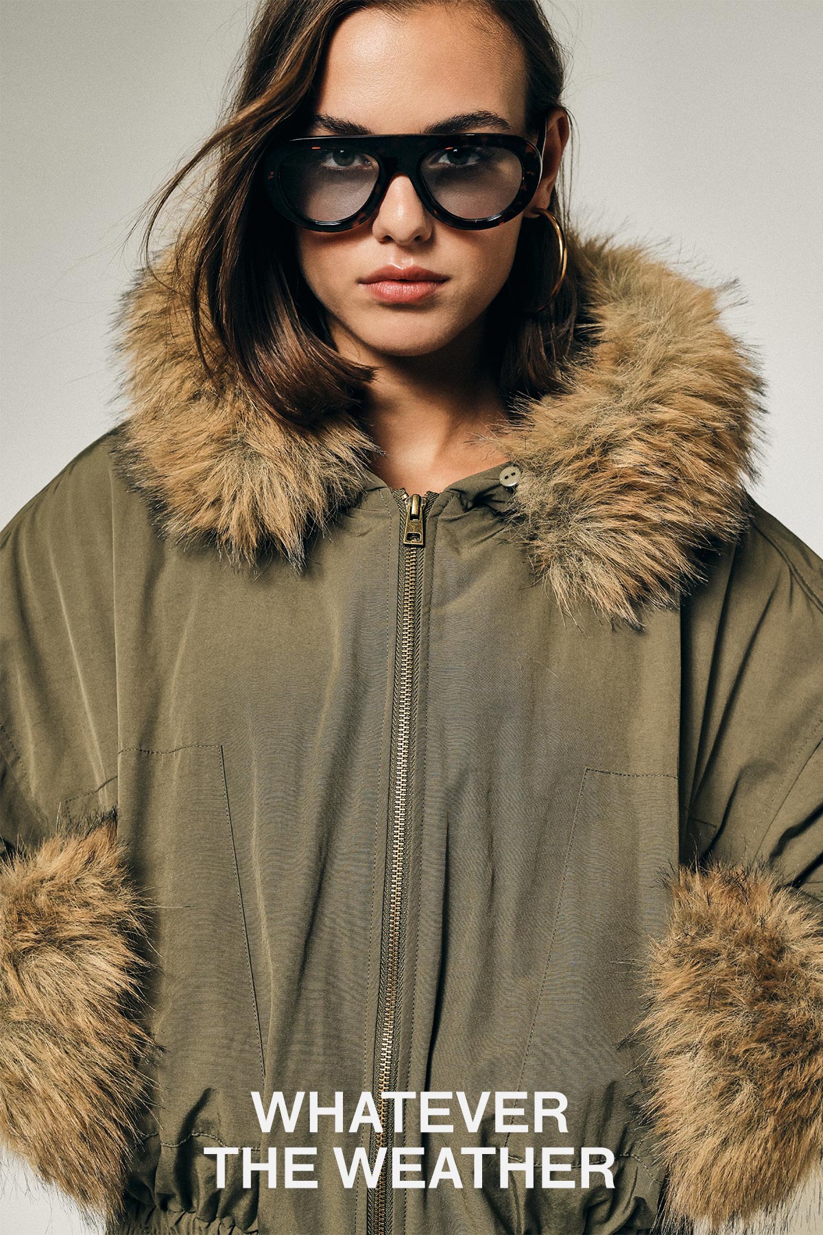 Model in olive parka with faux-fur hood and cuffs and oversized sunglasses; white text "WHATEVER THE WEATHER" on front
