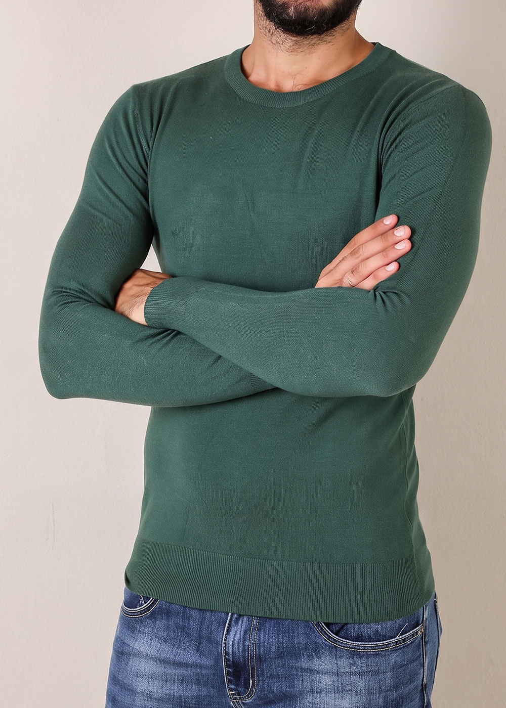 Male torso wearing slim-fit forest green long-sleeve jumper and blue jeans, arms crossed against a plain background