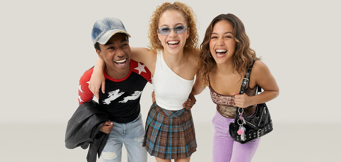 Tre giovani donne sorridenti che camminano insieme, indossando abiti casual colorati su uno sfondo chiaro uniforme.