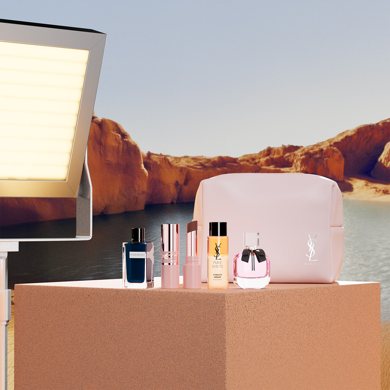 Una selezione di prodotti di bellezza YSL in miniatura e una trousse rosa chiaro esposti su un blocco di pietra in un canyon desertico.