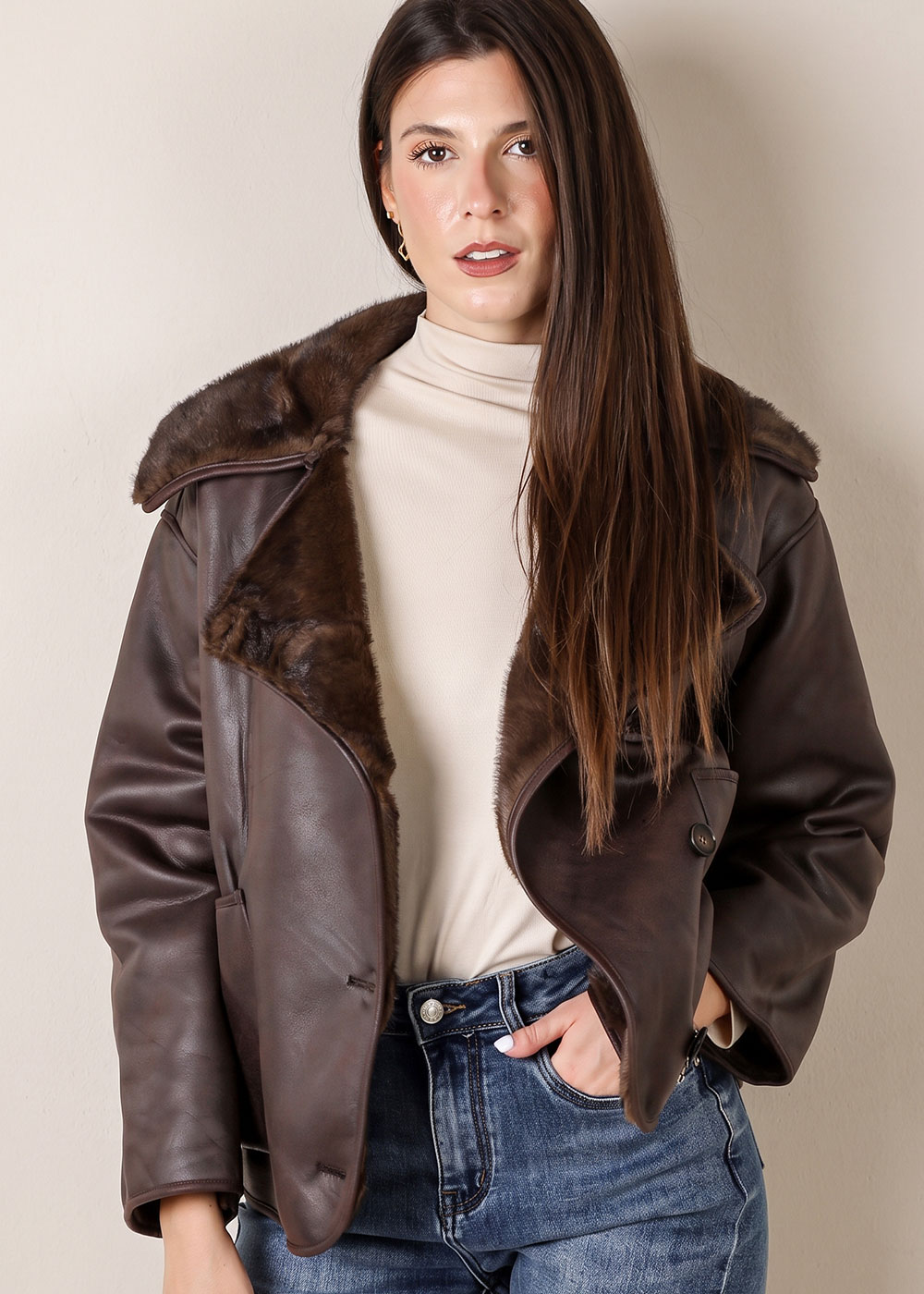 Woman modelling brown shearling leather jacket with cream roll-neck top and blue jeans, long straight hair, hand in pocket