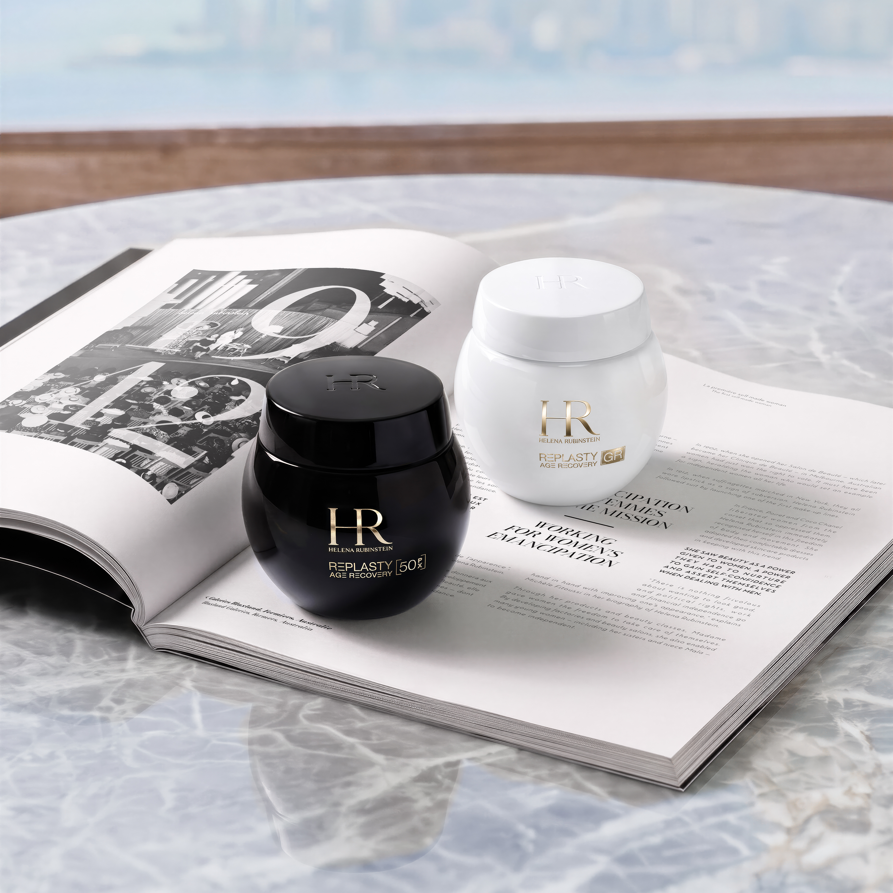 Duo di creme Helena Rubinstein Re-Plasty Age Recovery: la crema notte Night 50PX nel vasetto nero e la crema giorno Day [GR] nel vasetto bianco, adagiate sulle pagine aperte di un libro d'arte su un tavolo di marmo.