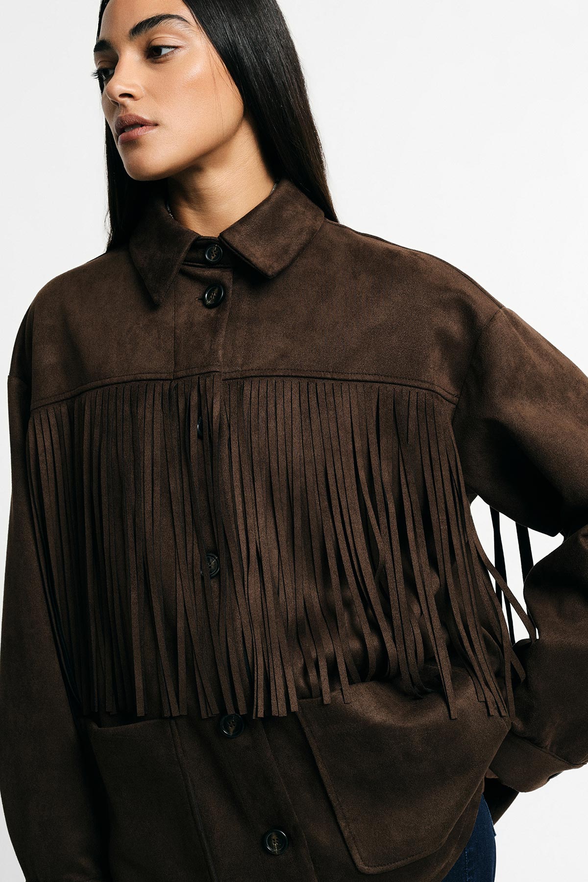 Female model wearing a brown suede fringe jacket with buttons, long dark hair in a three-quarter pose against a white background