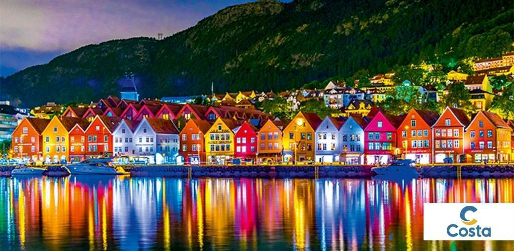 Colourful wooden houses of Bergen harbour at night, lit along the waterfront with boats and vivid reflections and a mountain backdrop