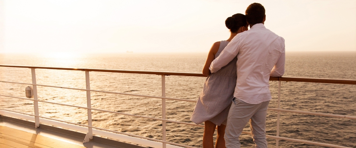 Couple embracing on a cruise ship deck at sunset, looking out over the calm sea