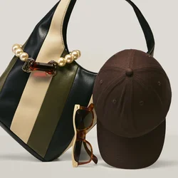 Borsa a righe con dettaglio di perle, cappellino da baseball marrone scuro e occhiali da sole tartarugati disposti su una superficie chiara e semplice.