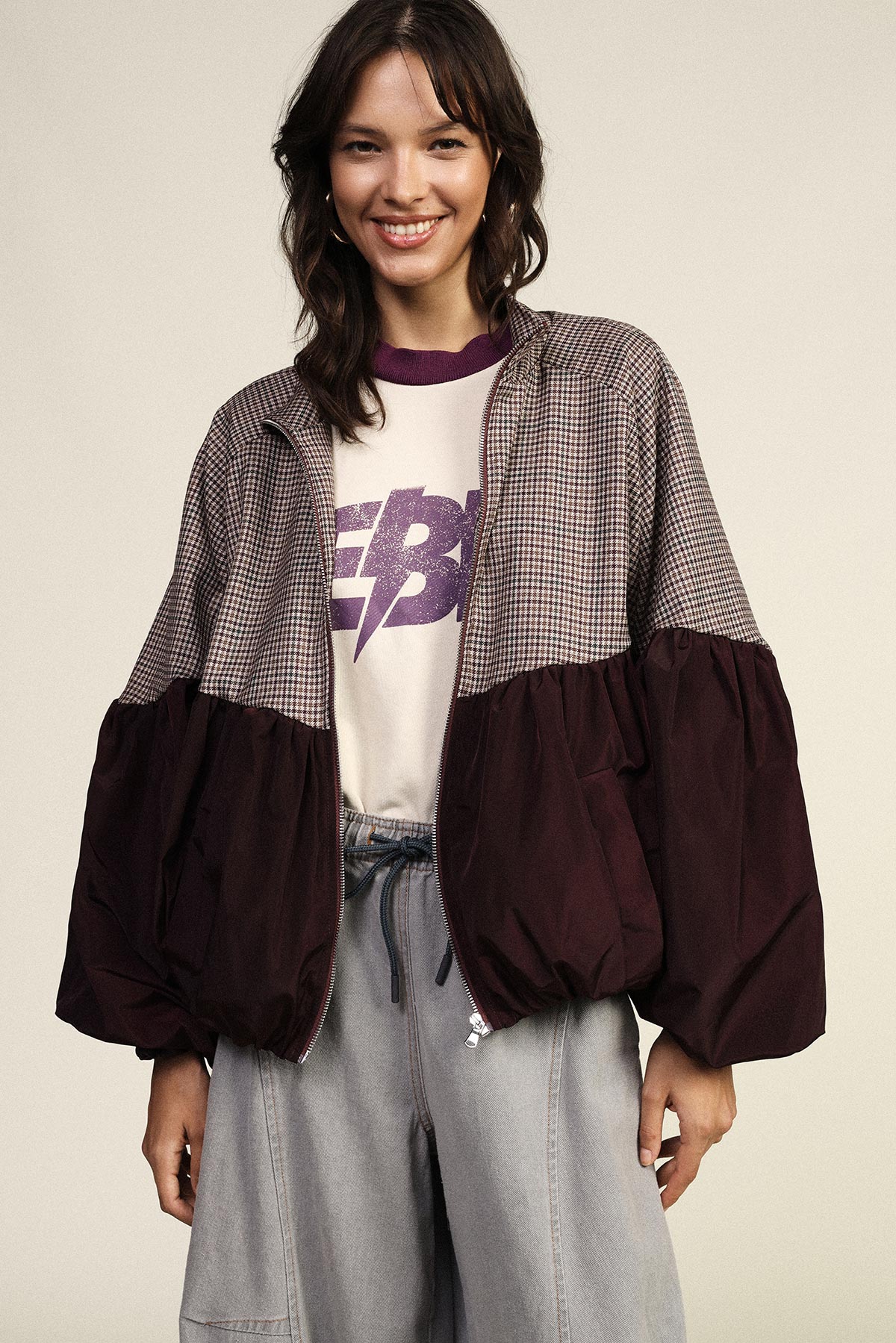 Smiling female model in oversized burgundy and houndstooth jacket, graphic tee and loose light-grey jeans, casual fashion look