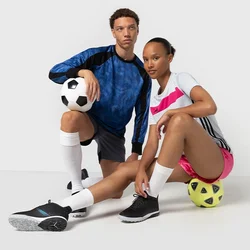 Due atleti in abbigliamento sportivo posano con palloni da calcio. L'uomo indossa una maglietta blu e nera, pantaloni neri e scarpe nere. La donna indossa una maglietta bianca con dettagli rosa e pantaloni corti.