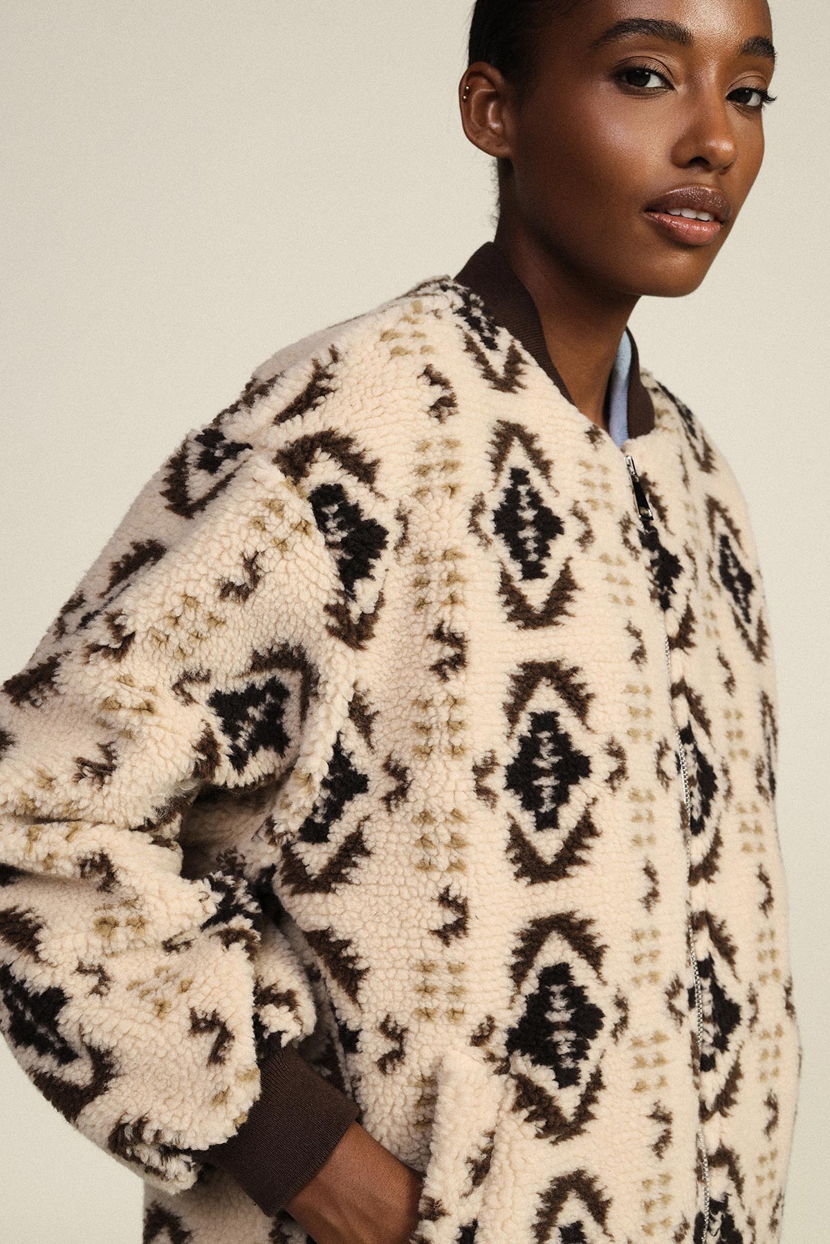 Woman wearing cream sherpa fleece bomber jacket with black geometric tribal print, close-up of textured fabric and zip
