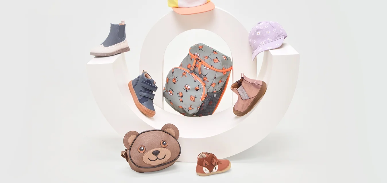 Accessori per bambini esposti: uno zaino grigio con motivo floreale, vari cappelli in colori pastello e scarpe in toni Terre, compresa una borsa a forma di orso.