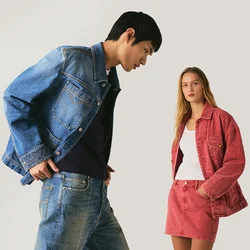 Giovane uomo con giacca di denim blu e jeans guarda verso il basso mentre donna con giacca di denim rossa e gonna guarda avanti su sfondo uniforme.