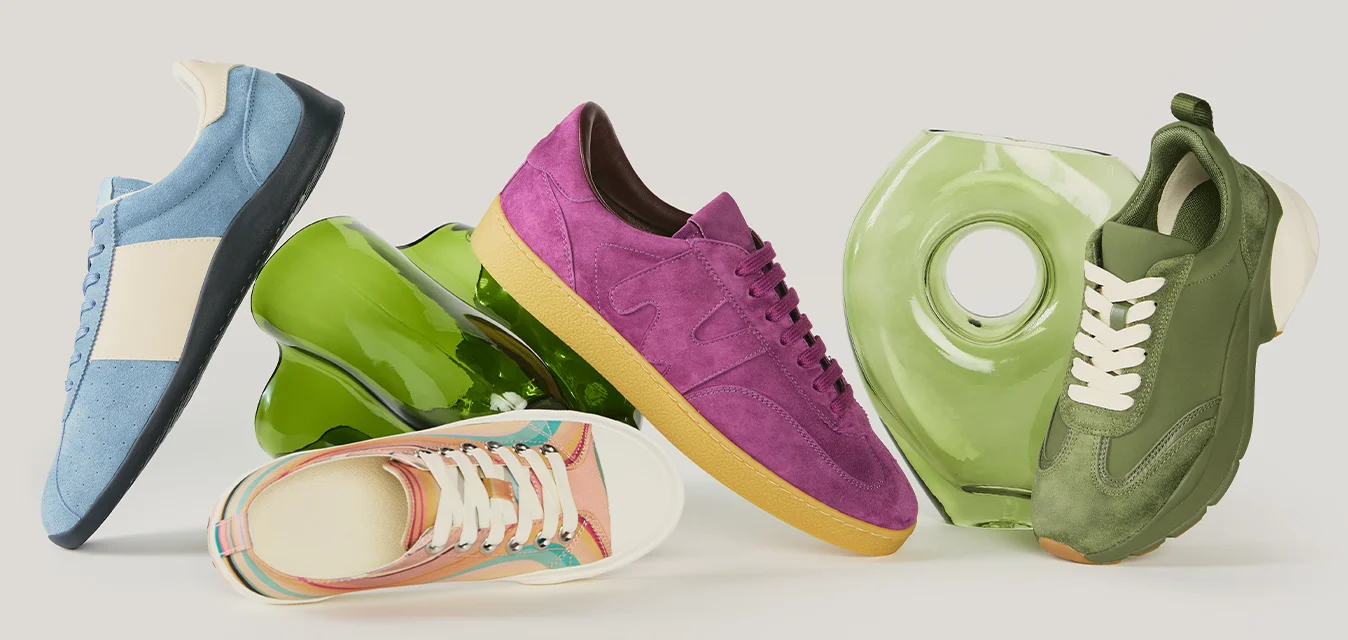 Quattro sneaker colorate in blu, rosa, multicolore e verde disposte in piedi con due bottiglie di vetro verdi su uno sfondo neutro.