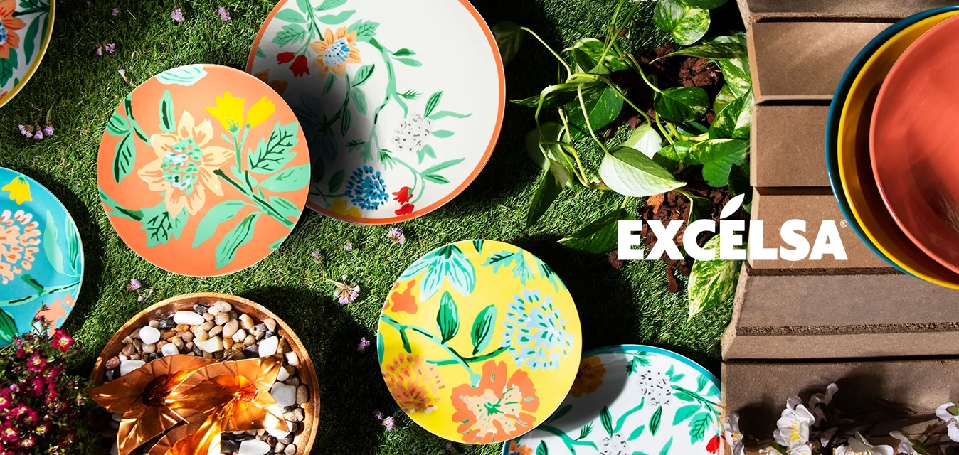 Piatto in ceramica colorati con motivi floreali in blu, giallo, arancione e bianco, disposti su erba verde con pietre decorative e piante.