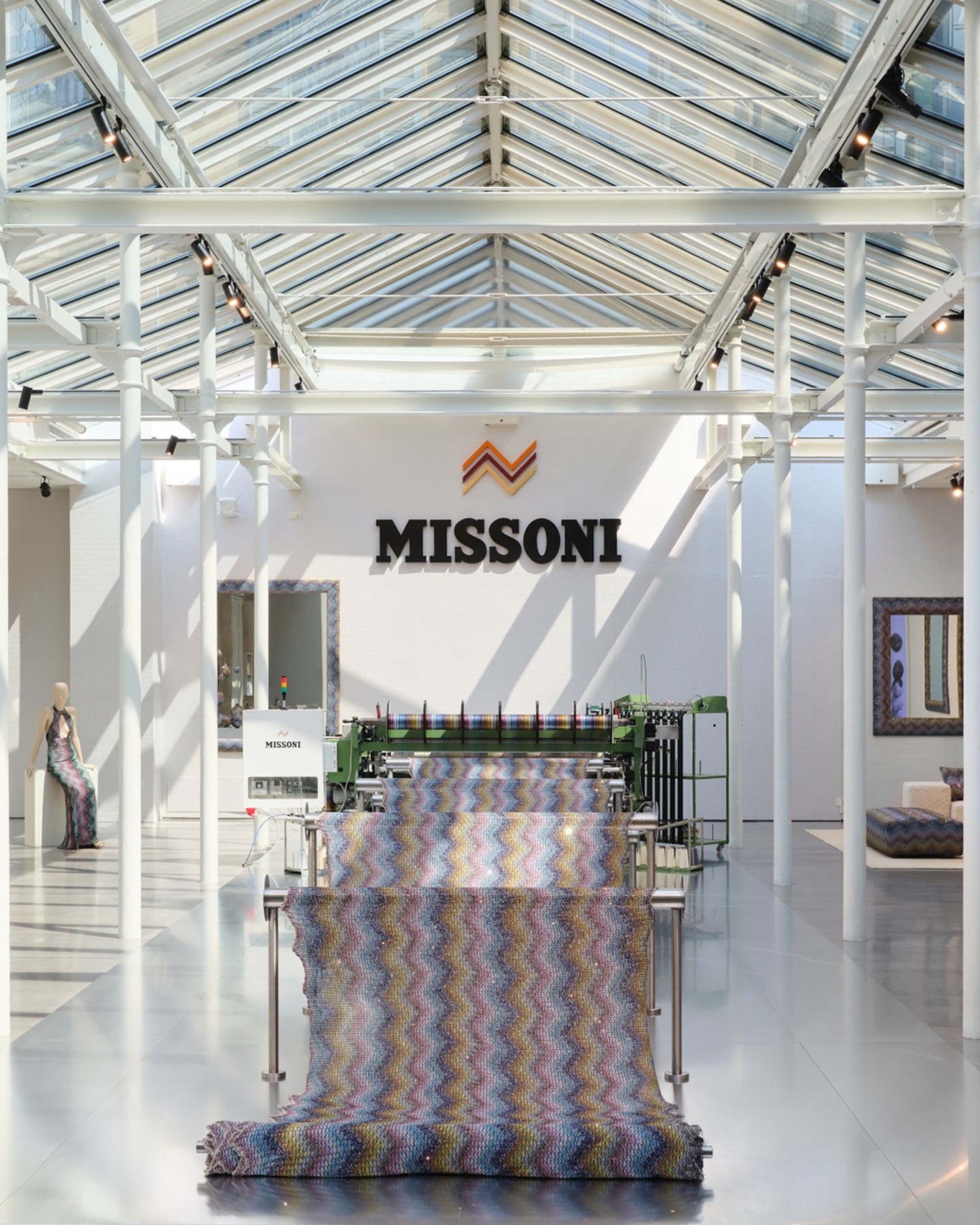 Bright Missoni showroom with skylight, knitting machine producing multicoloured zigzag fabric roll and mannequin
