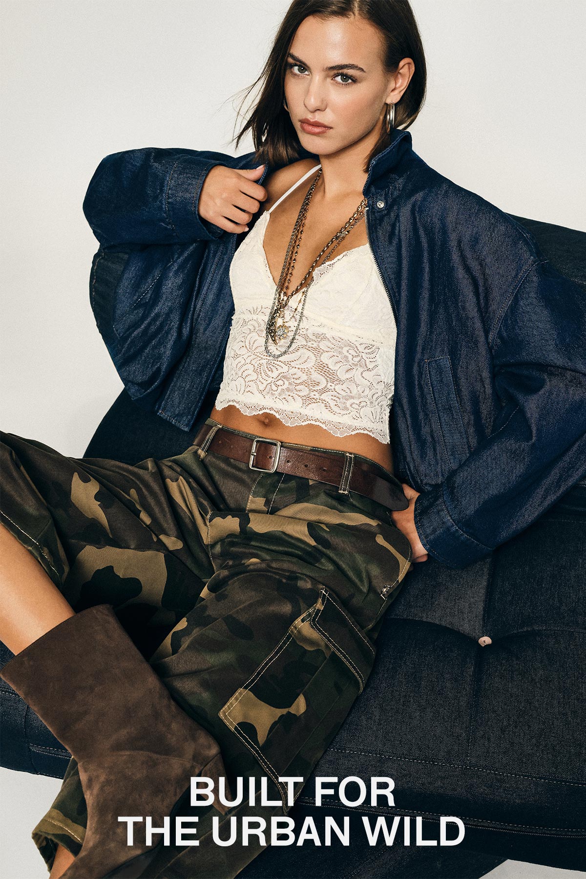 Woman on sofa wearing lace crop top, navy jacket, camouflage cargo trousers and brown boots; text 'BUILT FOR THE URBAN WILD'