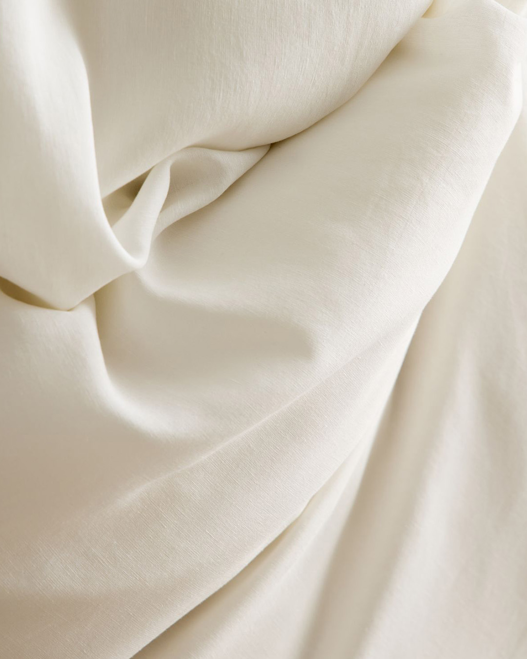 Close-up of cream-coloured fabric draped in soft folds, showing smooth, fine texture suitable for bedding, curtains or upholstery