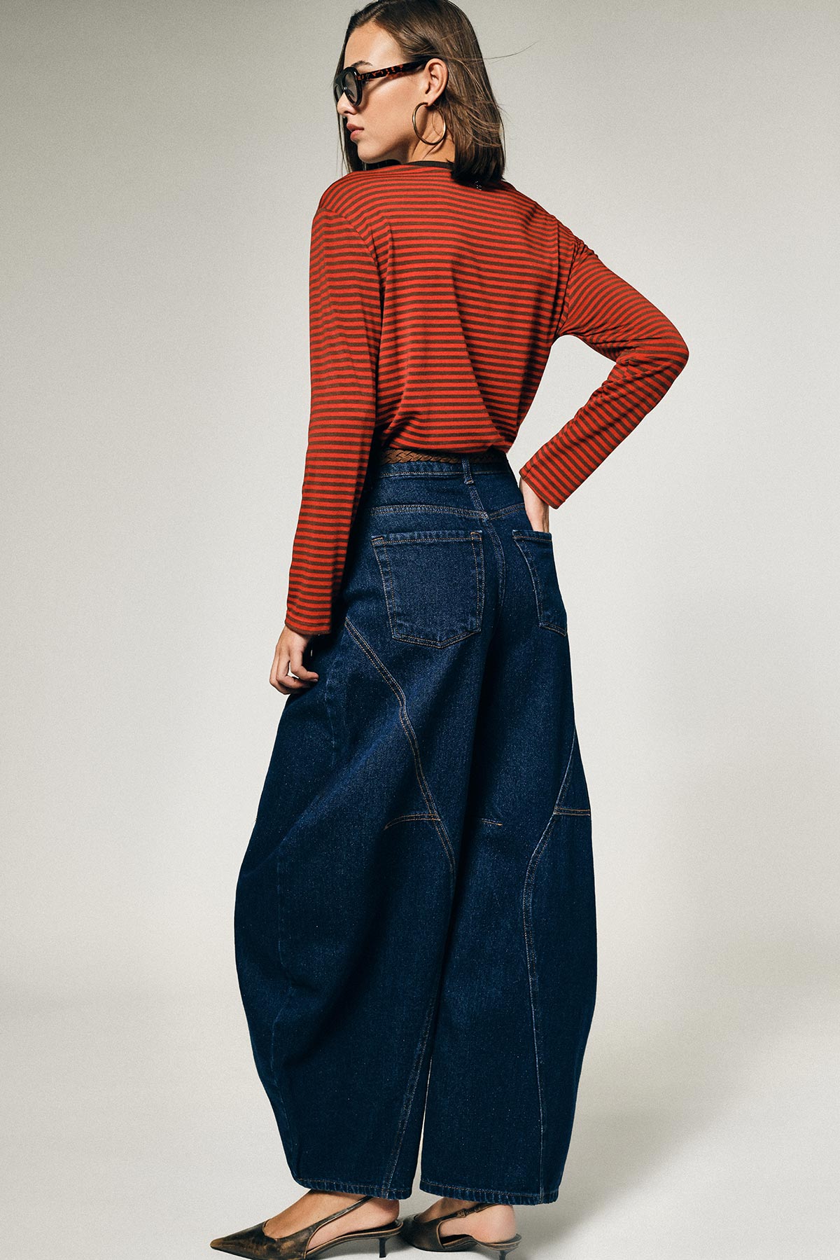 Model viewed from back wearing red striped long-sleeve top, oversized wide-leg dark denim jeans, sunglasses and hoop earrings