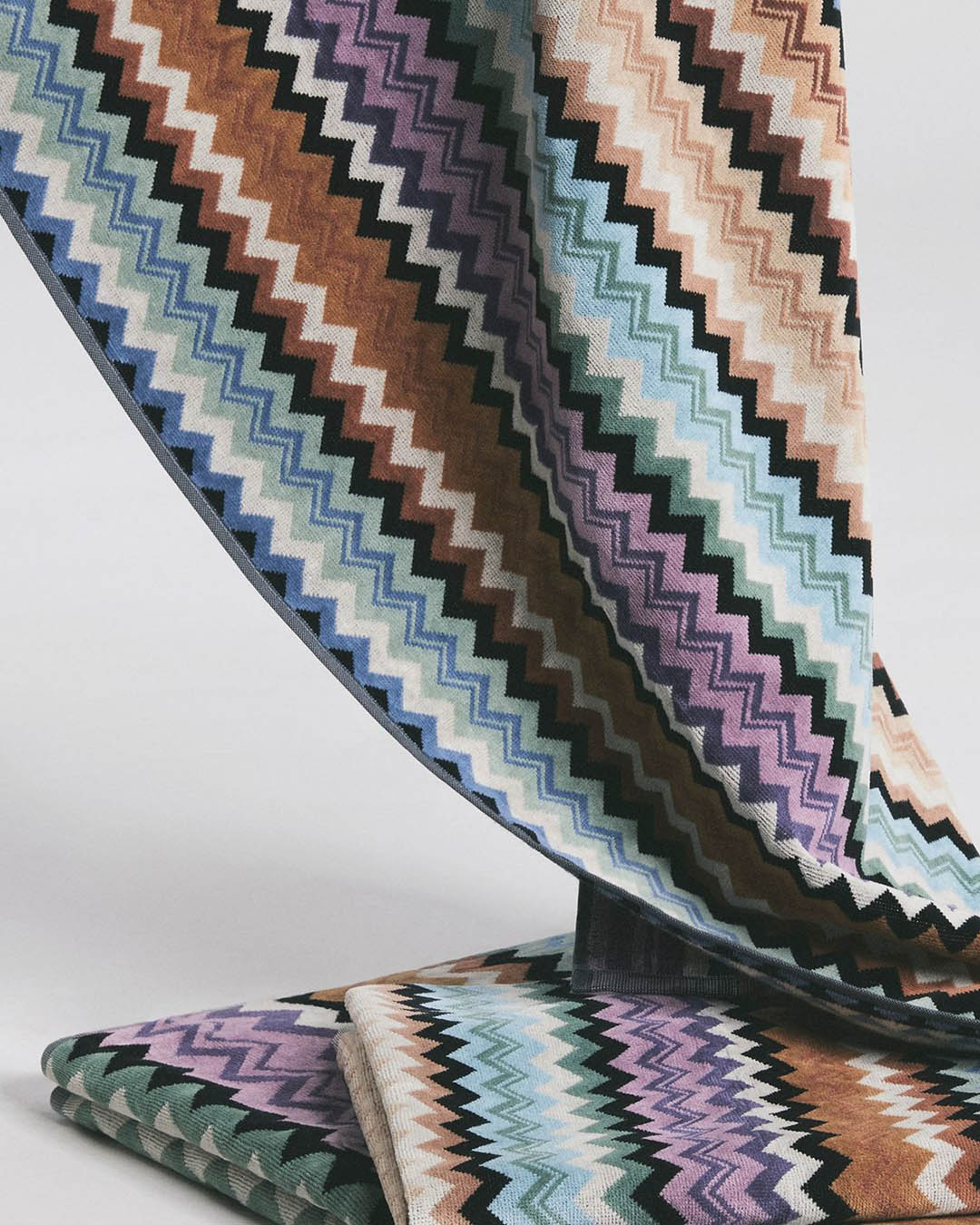 Multicolour zigzag (chevron) woven fabric draped and folded, pastel blues, greens, purples and browns