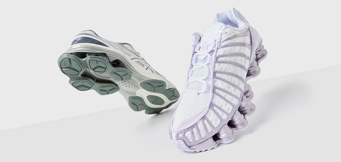 Due scarpe sportive: una bianca con accenti lavanda, parte superiore in rete e suola testurizzata; l'altra grigia, con un design elegante e suola in gomma.