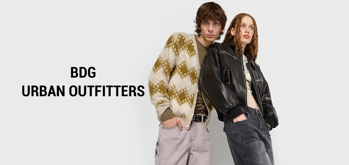 Due modelli posano davanti a uno sfondo bianco; uno indossa un maglione oversize a fantasia e pantaloni grigi, l'altro una giacca di pelle nera e pantaloni scuri.