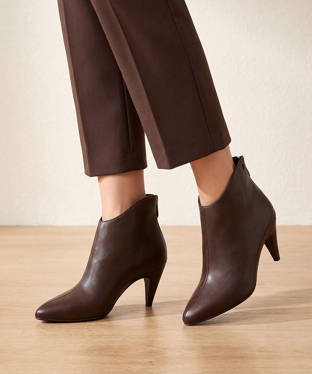 Woman wearing brown leather ankle boots with pointed toes and mid heels, styled with cropped brown trousers