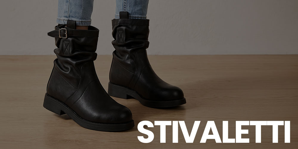 Black leather ankle boots with slouchy shaft and buckle strap, worn with light blue jeans on wooden floor, studio shot