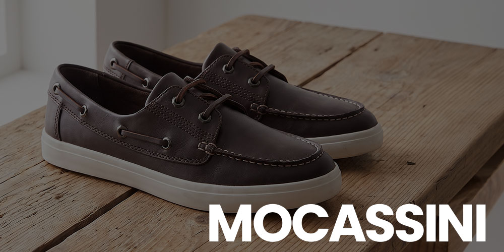 Pair of brown leather moccasins (boat shoes) with white rubber soles on a rustic wooden bench, 'MOCASSINI'