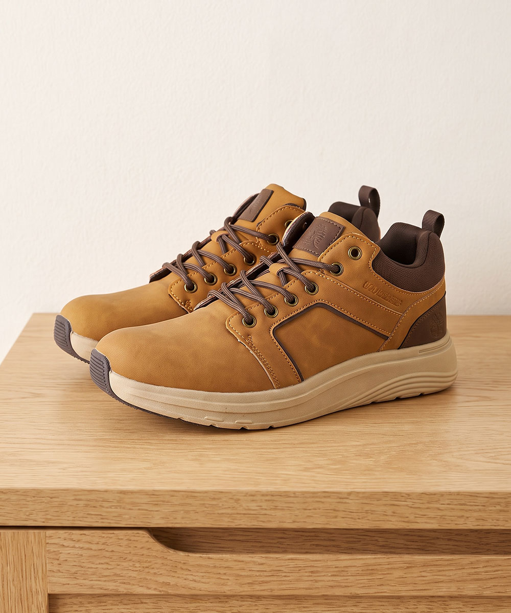 Pair of tan leather casual trainers with brown accents on a wooden table, laced and side view