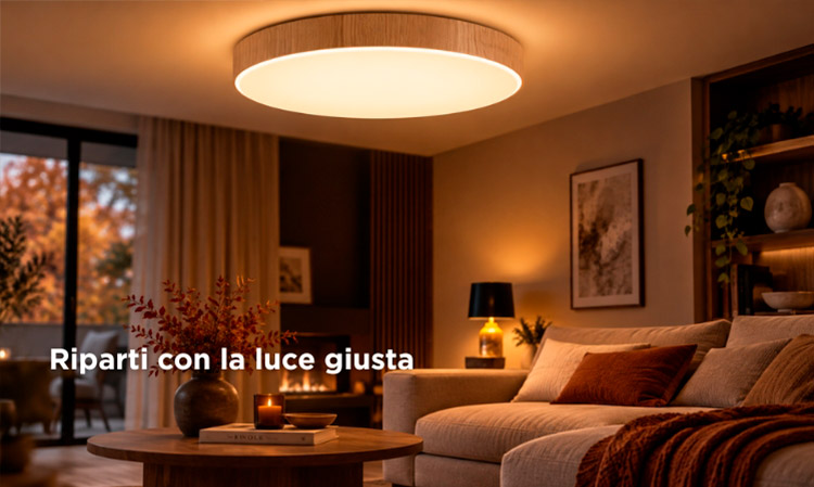 Warmly lit modern living room with large circular ceiling light, beige sofa, wooden coffee table and autumnal view through sliding doors