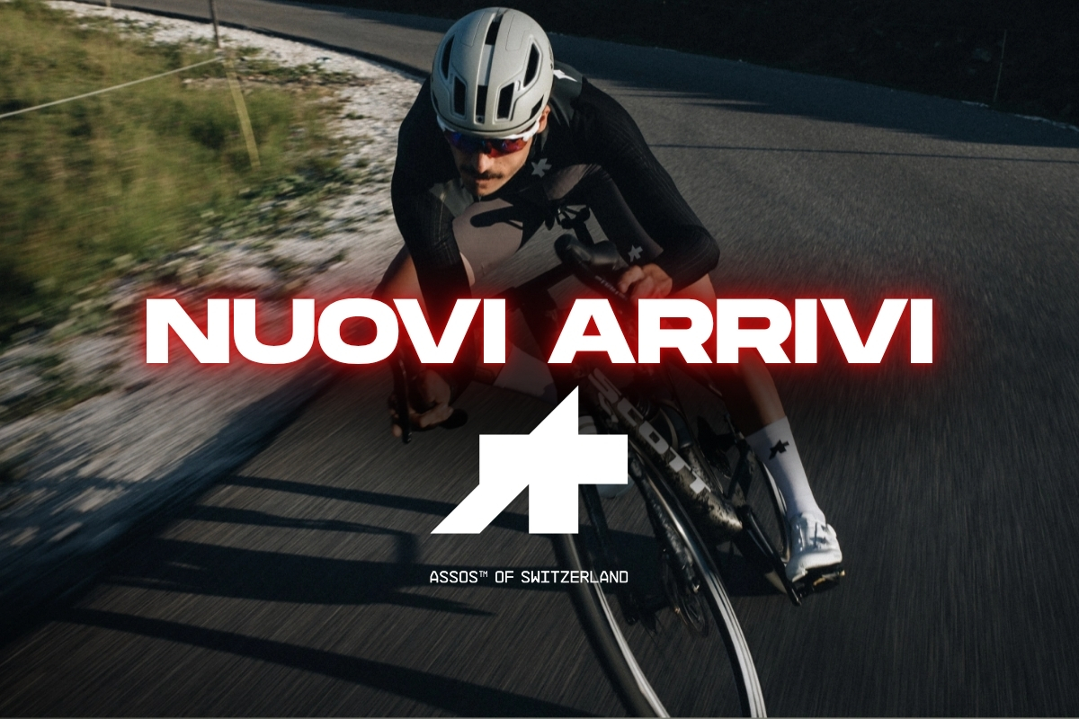 Cyclist cornering on a road bike in helmet and kit with overlay text 'NUOVI ARRIVI' and ASSOS of Switzerland logo — new arrivals cycling gear