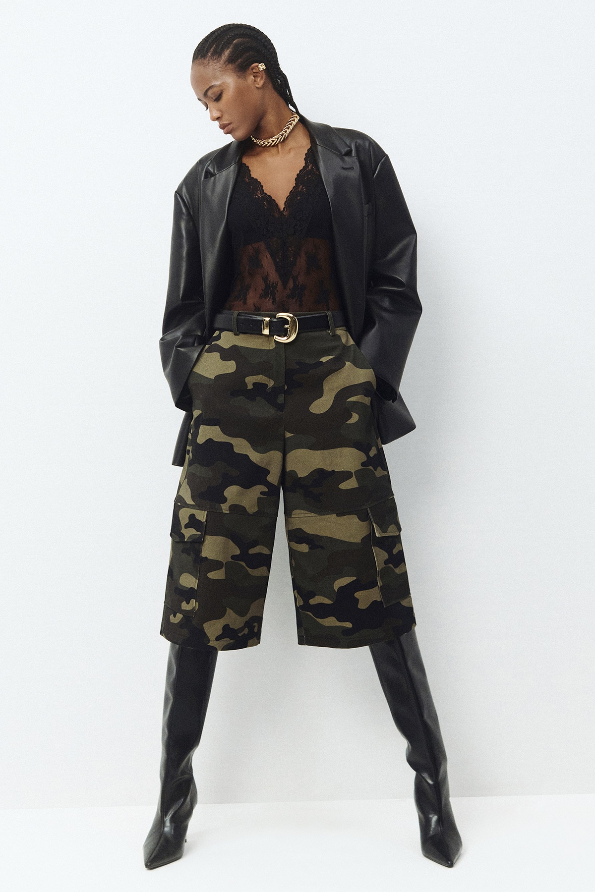 Woman modelling black leather blazer, lace bodysuit, camo cargo knee-length shorts, gold chain necklace and tall black boots