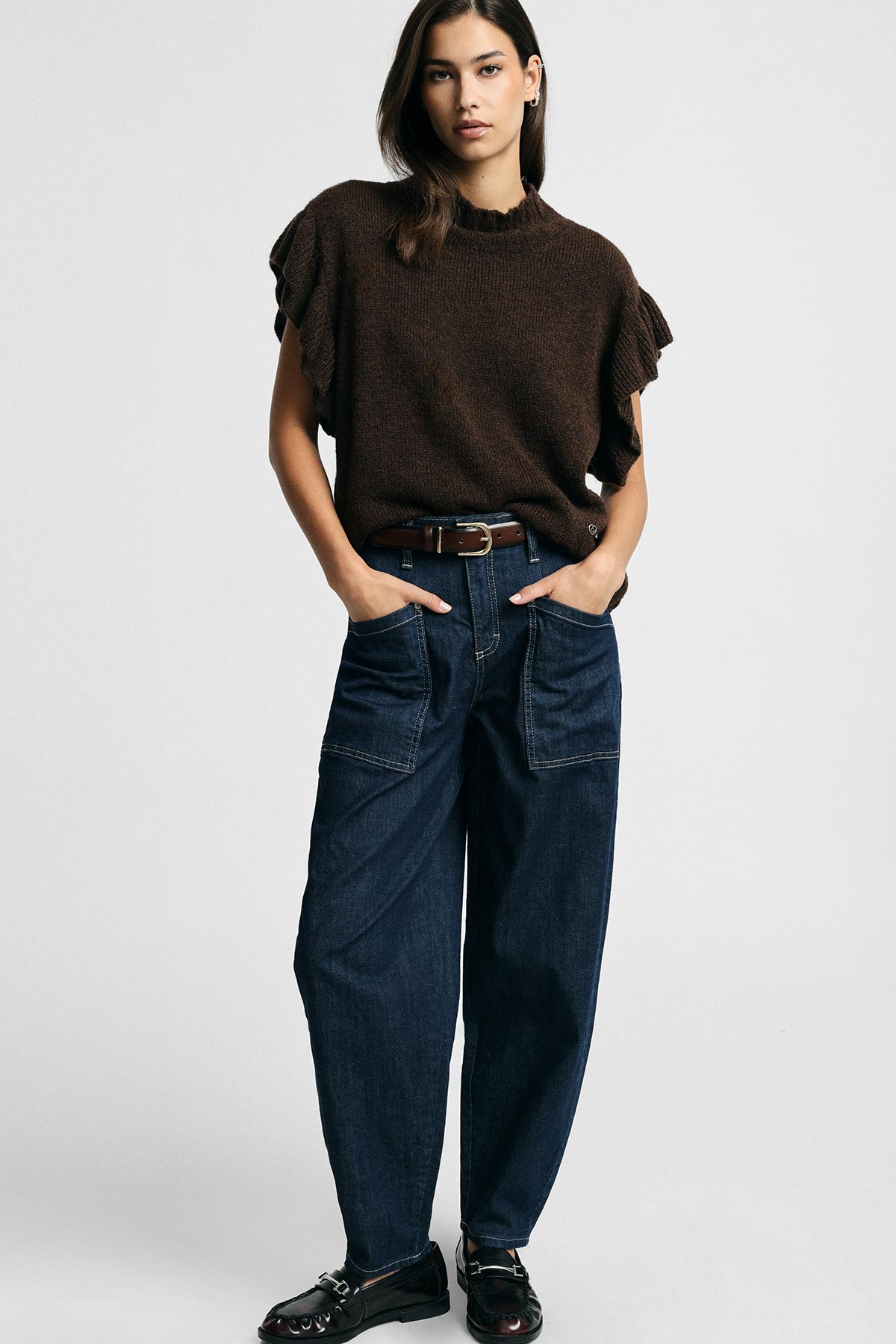 Model wearing brown knit ruffle-sleeve top, high-waist wide-leg dark denim jeans, belt and black loafers, hands in pockets