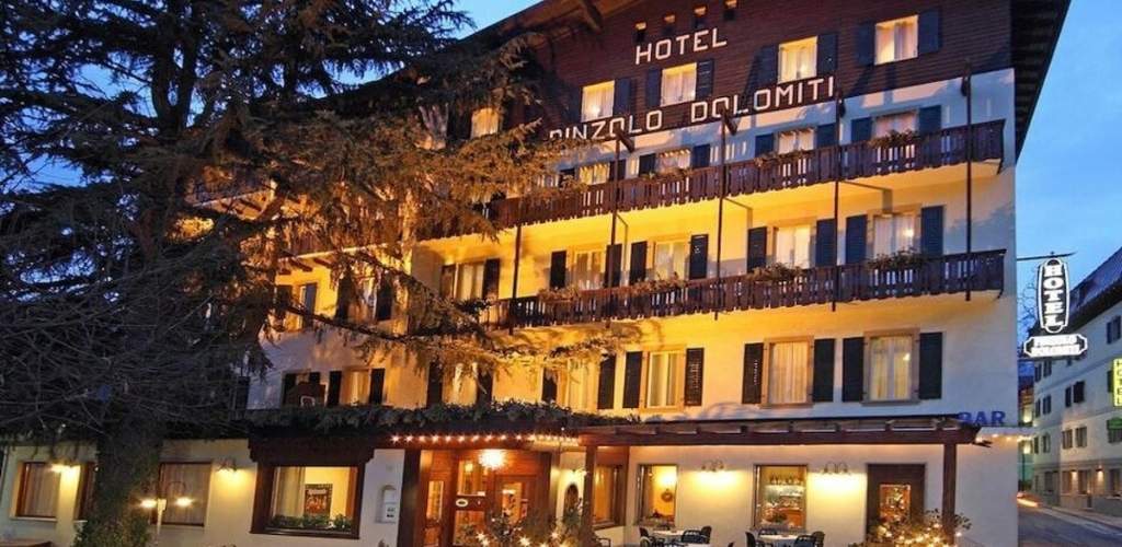 Exterior of Hotel Pinzolo Dolomiti at dusk, illuminated alpine façade with wooden balconies and warm entrance lights