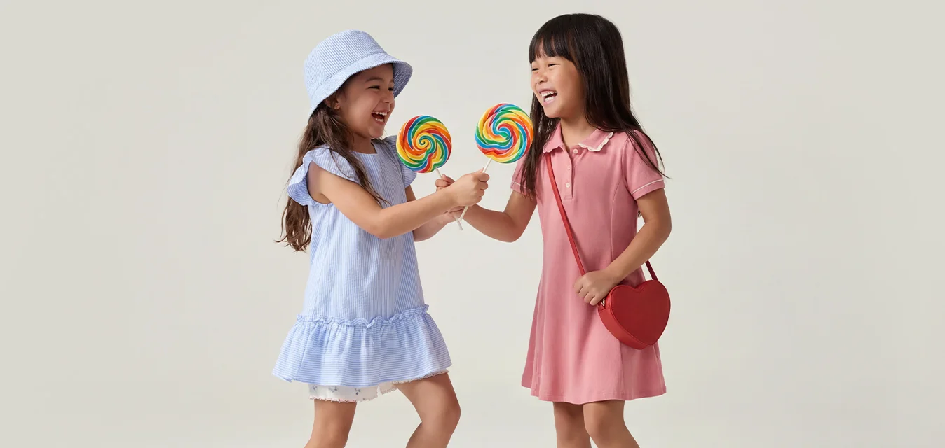 Due ragazze giovani sorridenti che tengono lecca-lecca colorati a spirale mentre si guardano l'una di fronte all'altra su uno sfondo semplice e chiaro.