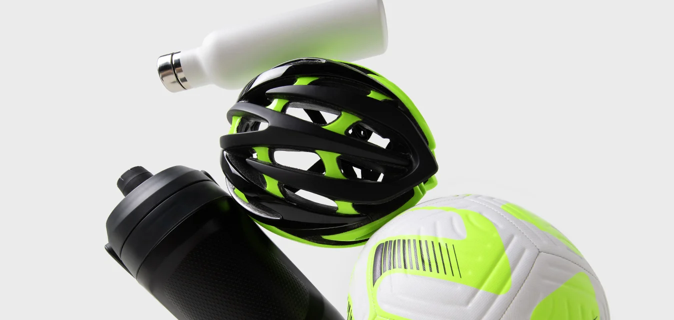 L'attrezzatura sportiva include un casco nero e verde neon, una bottiglia d'acqua nera e un pallone da calcio bianco e verde neon.