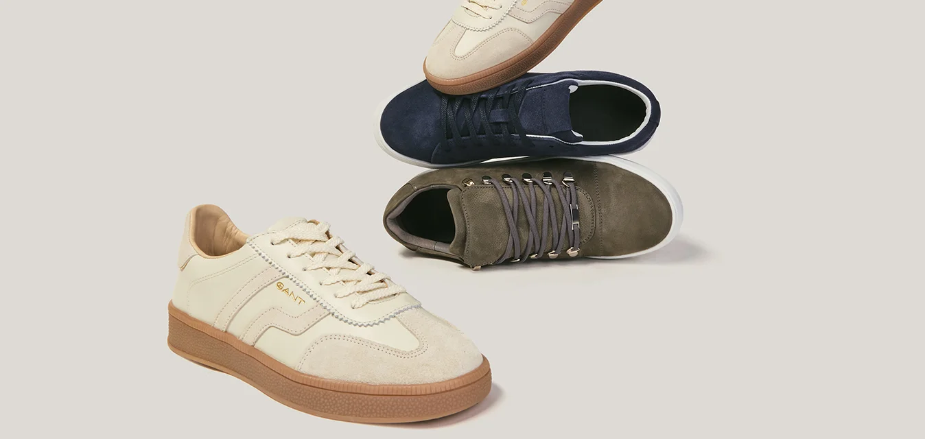 Tre paia di sneaker casual di colore beige, blu navy e verde oliva disposte su uno sfondo chiaro.