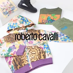 Giacca a vento colorata con motivi floreali, sneakers nere, pantaloni olivastri e magliette grafiche disposte su un supporto bianco curvo.