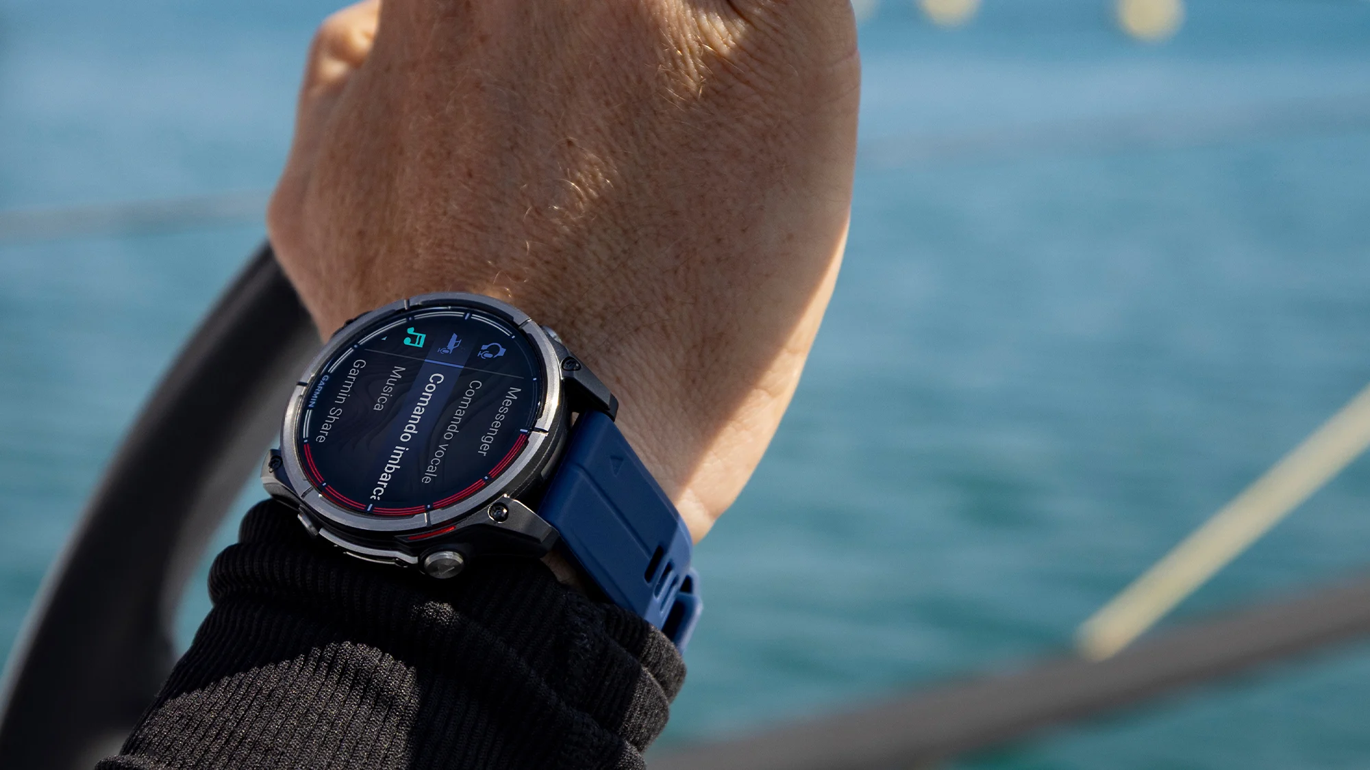 Mano sulla ruota del timone con il Garmin Quatix 8 al polso, mare sullo sfondo
